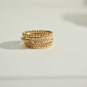 Puede incluir: Un conjunto de seis anillos apilables de oro con diferentes texturas y patrones. Los anillos están apilados uno encima del otro, creando un look único y elegante.