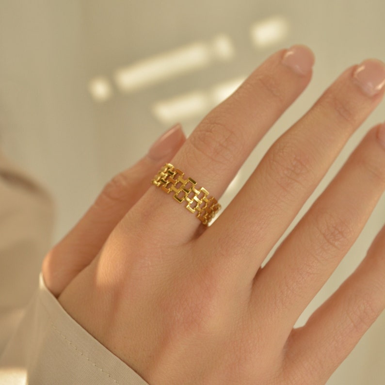 May include: A gold ring with a geometric design. The ring is made of a series of interlocking squares.