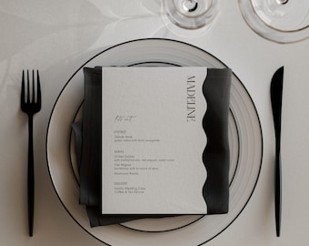May include: A black and white wedding menu card with the text "trat" and "MADELINE" on a white plate with a black napkin. The menu includes salad, salmon, flat mignon, mushroom risotto, vanilla wedding cake, coffee, and tea.