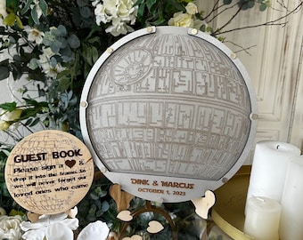 May include: A wooden guest book shaped like the Death Star from Star Wars. The book is on a stand with a sign that says "Tink & Marcus, October 1, 2023".