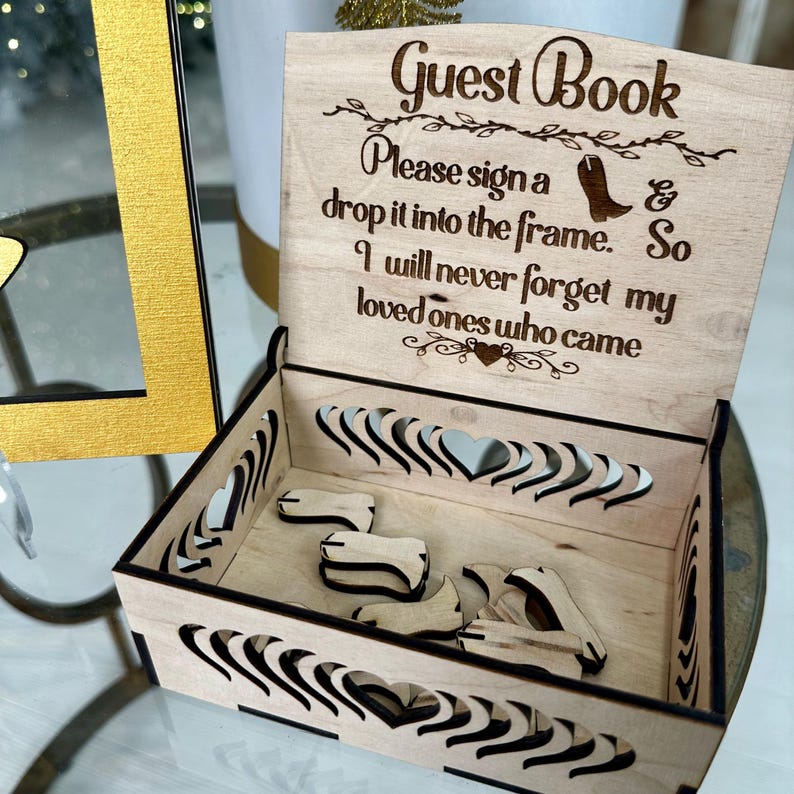May include: Wooden guest book box with a cutout design of hearts. The lid has a sign that reads "Guest Book Please sign a & drop it into the frame. So I will never forget my loved ones who came".