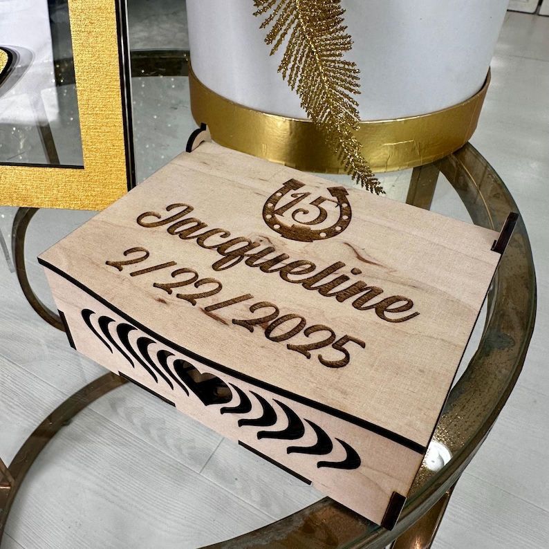 May include: A wooden box with a horseshoe design and the text "Jacqueline 21221/2025" engraved on the top.