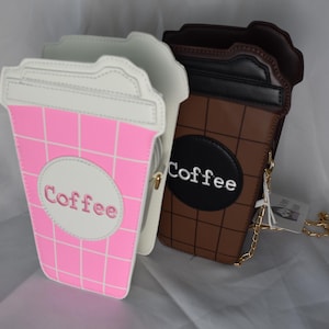 May include: Two coffee cup shaped purses, one pink and white and one brown and black, with the word "Coffee" embroidered on each. Both purses have a gold chain strap.