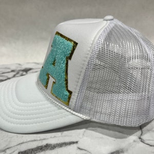 May include: White trucker hat with a light blue and gold letter 'A' on the front.