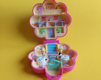 May include: A vintage pink and yellow miniature playset shaped like a flower, featuring a restaurant scene. The playset includes small tables, two figures, and a kitchen area. The interior has a detailed design with miniature furniture and accessories.