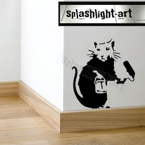 May include: Black and white wall decal featuring a rat holding a paint roller and a can of paint. The rat is depicted in a stencil art style, with the text "T" on the paint can. The decal is applied to a white wall.