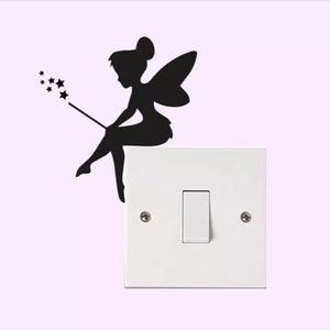 May include: A black silhouette of a fairy with a wand and stars, perched on a white light switch. The fairy has wings and is in a sitting position. The background is a light purple color.