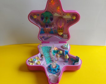 Könnte beinhalten: Ein rosa sternförmiges Spielzeug-Set, geöffnet, um einen Miniatur-Vergnügungspark zu zeigen. Zu den Merkmalen gehören ein Riesenrad, ein Heißluftballon und kleine Figuren. Der Innenraum ist mit verschiedenen Strukturen und Lichtern detailliert.