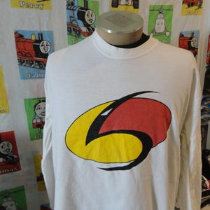 Peut inclure: T-shirt à manches longues blanche avec un motif graphique rouge, jaune et noir d'un numéro 6 stylisé. Le graphique est sur le devant du t-shirt.