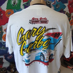 May include: White t-shirt with a colorful graphic of race car driver Gary Garby #99. The graphic includes the text "Gary Garby" and "Larry Shaw".