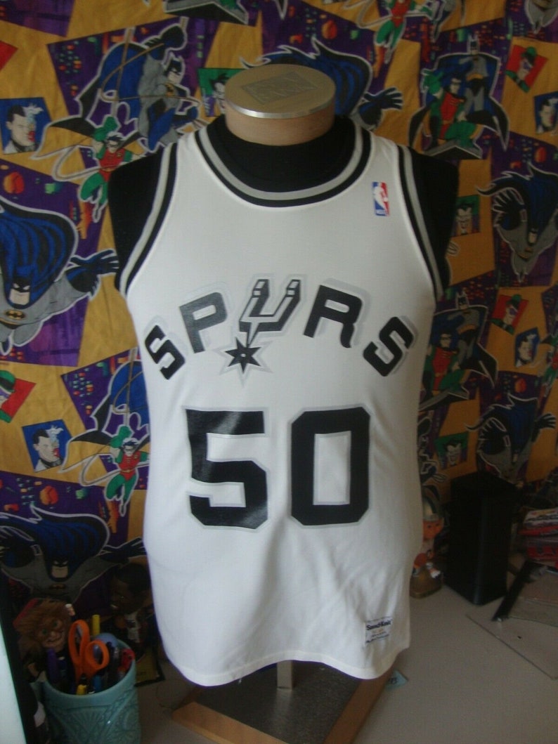 May include: White basketball jersey with black and silver lettering. The jersey says "SPURS" and "50".