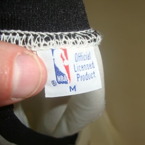 May include: White tag with blue text that reads "Official Licensed Product" and "NBA" logo. The tag also has a size "M" printed on it.