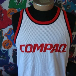 May include: White basketball jersey with red trim and the word "COMPAQ" in red lettering.