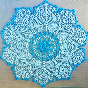 May include: A white crocheted doily with a blue centre. The doily has a scalloped edge and a delicate floral pattern.