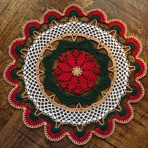May include: A white crocheted doily with a red, green and gold poinsettia design in the centre. The doily has a scalloped edge with red, green and gold accents.