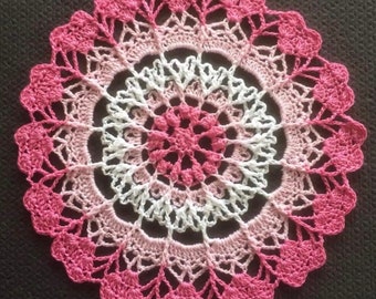 Peut inclure: Un napperon crocheté rose et blanc avec un motif floral délicat. Le napperon est réalisé avec un dégradé de fil rose, partant d'un rose plus foncé au centre et s'estompant vers un rose plus clair sur les bords.