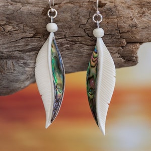 May include: A pair of silver feather earrings with iridescent abalone shell accents. The earrings are a light ivory color and have a delicate, feminine design.