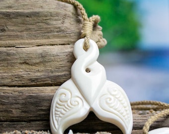 May include: White bone pendant carved in the shape of a fish tail with intricate designs. The pendant is attached to a natural fiber cord.