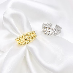 May include: Two open-style rings featuring a multi-row beaded design. One ring is finished in a bright gold tone, while the other is finished in a silver tone. Both rings are constructed from small, uniform metallic spheres arranged in a grid.