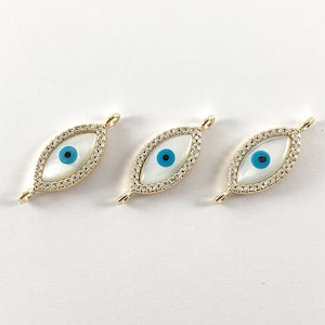 May include: Three gold evil eye charms with white mother of pearl and blue accents. The charms are set with clear rhinestones.