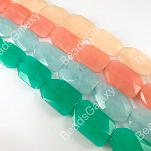May include: A strand of faceted gemstone beads in shades of green, blue, pink, and peach. The beads are rectangular and have a smooth, polished finish.