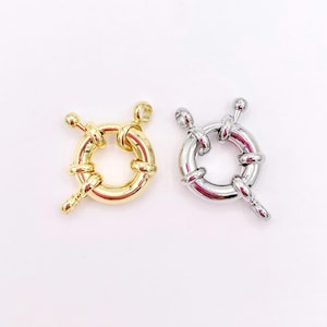 May include: Two circular jewelry clasps, one in a polished gold tone and one in a polished silver tone. Each clasp features a round ring body with a spring-loaded mechanism, a small protruding lever, and two attached loops for connecting to jewelry chains.