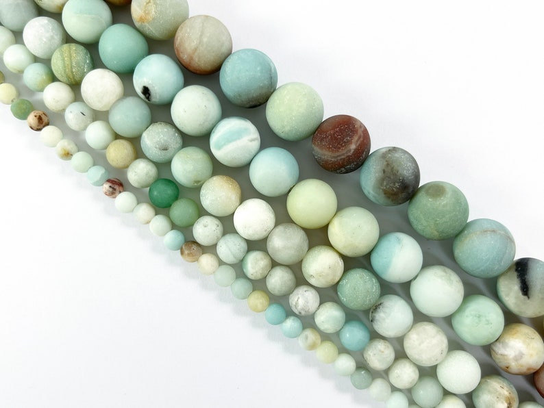 May include: A strand of round, smooth, green, white, and brown gemstone beads. The beads are various sizes and have a natural, polished finish.