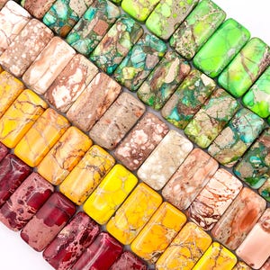 May include: A collection of colorful, rectangular, polished, natural stone beads. The beads are in various shades of green, brown, yellow, and red. The beads are arranged in a staggered pattern, creating a visually appealing display.
