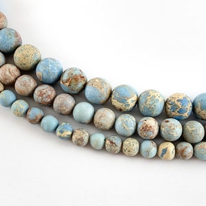 May include: A strand of blue, brown, and white marbled round beads. The beads are arranged in three rows, with the largest beads at the top and the smallest beads at the bottom.