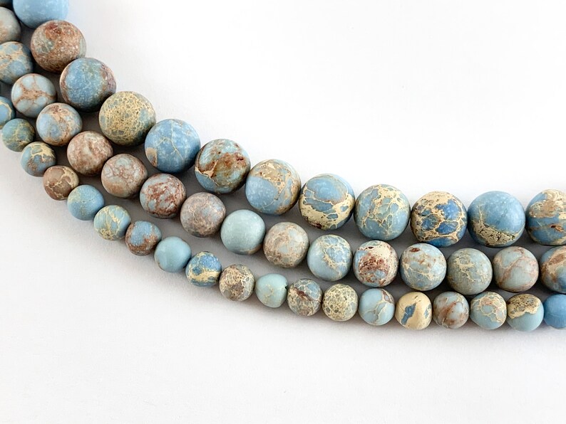 May include: A strand of blue, brown, and white marbled round beads. The beads are arranged in three rows, with the largest beads at the top and the smallest beads at the bottom.