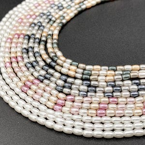 May include: A collection of pearl and glass beads in various colors, including white, pink, and gray. The beads are arranged in a circular pattern, creating a layered effect.