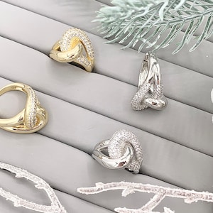 May include: Four silver and gold rings with clear cubic zirconia stones. The rings are displayed on a gray background.