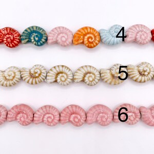 May include: Three rows of ceramic beads shaped like nautilus shells. The top row features red, blue, pink, orange, and light blue beads. The middle row has beige and brown striped beads. The bottom row consists of solid pink beads. Numbers 4, 5, 6.