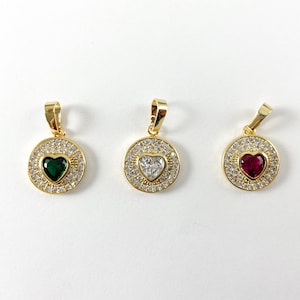 May include: Three gold pendants with a circle design and a heart-shaped stone in the center. The stones are green, clear, and red.
