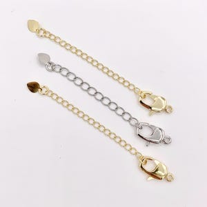 May include: Three necklace extender chains in gold and silver tones. Each chain has a heart-shaped end and a lobster clasp. The chains are designed to add length to necklaces and bracelets.