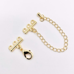 May include: Gold-colored jewelry findings, including a lobster clasp, chain, and two bar connectors. The connectors have three loops each. The chain is made of small, oval links. The findings are on a white background.