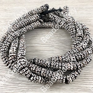 May include: A strand of black and white patterned wooden beads. The beads are round and have a raised design of small circles.