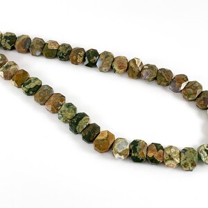 May include: A strand of green, brown, and white gemstone beads. The beads are faceted and have a unique, speckled pattern.
