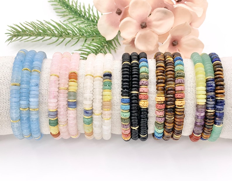 Peut inclure: Plusieurs bracelets de perles de diff&eacute;rentes couleurs, dont bleu clair, rose, blanc, noir, marron, jaune et vert. Chaque bracelet est compos&eacute; de petites perles plates s&eacute;par&eacute;es par des entretoises dor&eacute;es. Les bracelets sont pr&eacute;sent&eacute;s sur un tissu blanc.