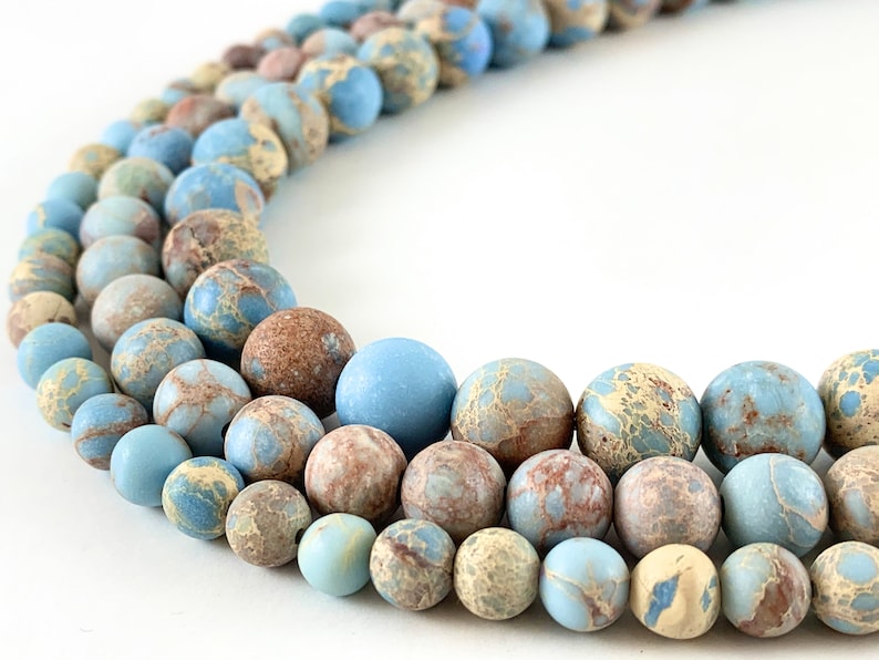May include: A strand of blue and brown marbled round beads. The beads are smooth and have a speckled pattern.