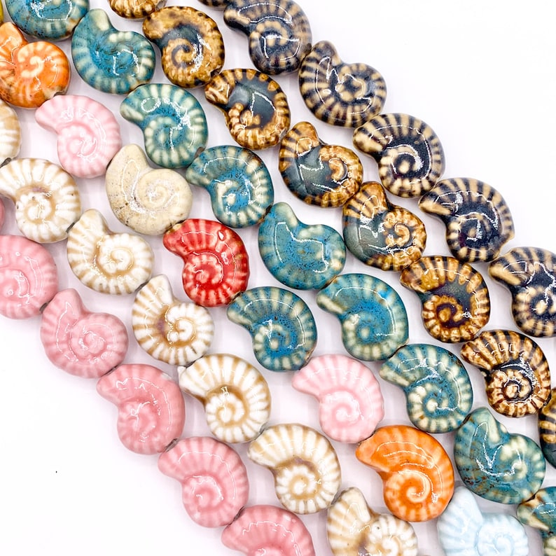 May include: A collection of ceramic beads shaped like nautilus shells, arranged in diagonal rows. The beads feature a glossy finish and a variety of colours including pink, orange, white, turquoise, brown, and dark blue, each with a spiral pattern.