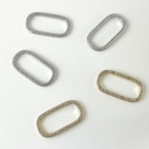 May include: Four oval-shaped metal connector charms with a clear rhinestone border. Two charms are silver, one is gold, and one is a lighter gold.