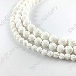 May include: White carved shell beads, round and smooth, with a floral design. The beads are strung together in a strand.
