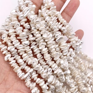 May include: Strands of irregular, off-white freshwater pearls. The pearls have a lustrous, slightly iridescent sheen. The beads are strung together, creating a flowing, organic texture. Ideal for jewelry making, these pearls offer a unique, natural aesthetic.