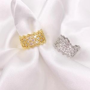 May include: Two wide bands, one gold-toned and one silver-toned, featuring an intricate lattice or mesh design. Each band is encrusted with numerous small, clear, sparkling stones set within the textured metal framework of the ring structure.