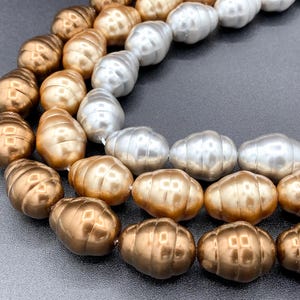 May include: A strand of faux pearls in three colors: gold, silver, and a darker bronze. The pearls are large and have a slightly irregular shape.