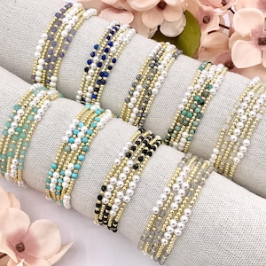 May include: A set of eight beaded bracelets with gold accents. The bracelets feature different colored beads, including turquoise, black, white, and gray.