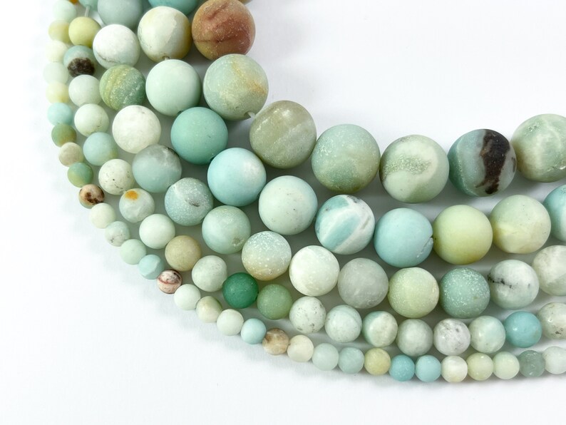 May include: A collection of smooth, round, green and white amazonite beads of various sizes. The beads are arranged in a semi-circle, with the largest beads at the top and the smallest beads at the bottom.