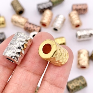 May include: Assortment of metal beads in various finishes, including gold, silver, and brass. The beads have a hammered texture and are cylindrical in shape.