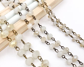 May include: A strand of white faceted glass beads strung on a brass chain. The beads are round and have a slight iridescent sheen.